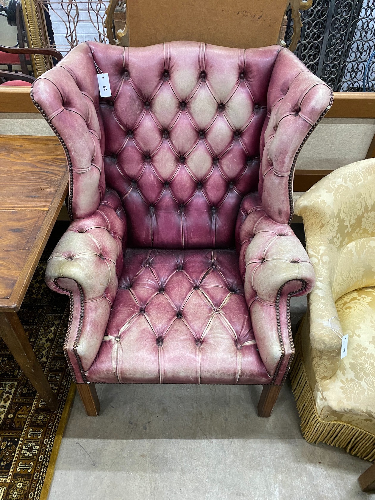 A George III style button back wing armchair upholstered in faded burgundy buttoned leather, width 82cm, depth 82cm, height 110cm